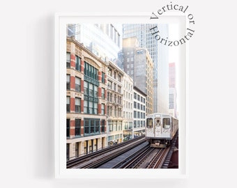 May include: A white train travelling on elevated tracks in a city with tall buildings. The train is travelling towards the viewer. The buildings are brick and glass.