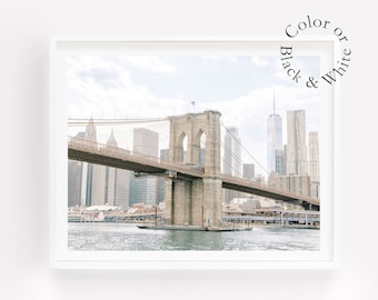 May include: A black and white photograph of the Brooklyn Bridge in New York City. The bridge is a suspension bridge with a large arch in the center. The bridge is surrounded by tall buildings and the water.