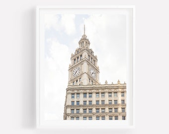 May include: A close-up view of a tall, ornate building with a clock tower. The building is made of light-coloured stone and has many windows. The clock face is visible on the tower, and the sky is a light blue with some clouds.