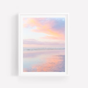 May include: A photograph of a beach at sunset with pink and purple clouds reflected in the water.