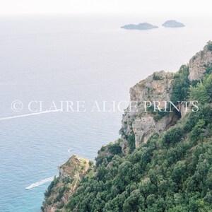 May include: A panoramic view of a rocky cliffside covered in lush green trees overlooking a vast blue ocean. Two small islands are visible in the distance.