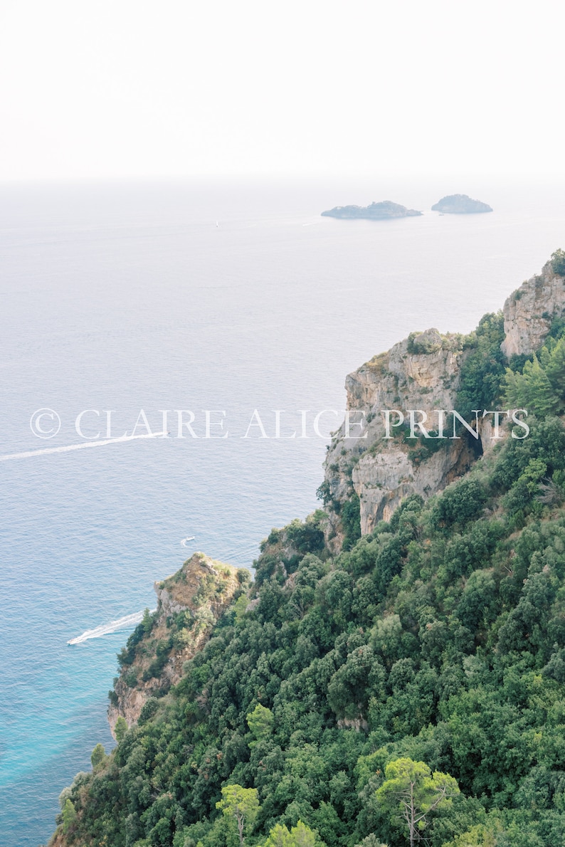 May include: A panoramic view of a rocky cliffside covered in lush green trees overlooking a vast blue ocean. Two small islands are visible in the distance.