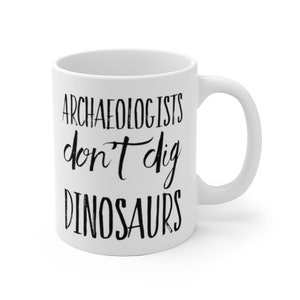 May include: White ceramic coffee mug with black text that reads "Archaeologists don't dig dinosaurs".