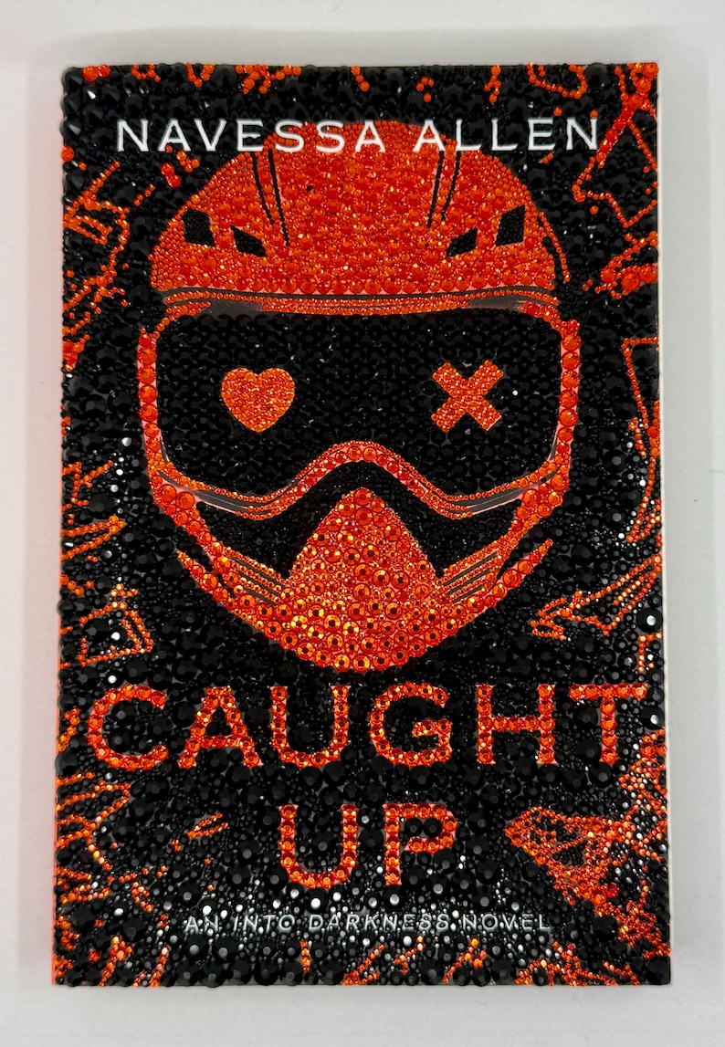 May include: A book cover with the title "CAUGHT UP" and the author's name "NAVESSA ALLEN". The cover features a black background with an orange graphic of a helmet and goggles, and the text is also orange.