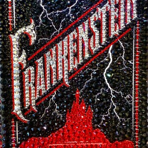 May include: A black and red embellished cover of "Frankenstein" by Mary Shelley. The title and author's name are in sparkling crystals. The background is black with white lightning bolts and a red castle.