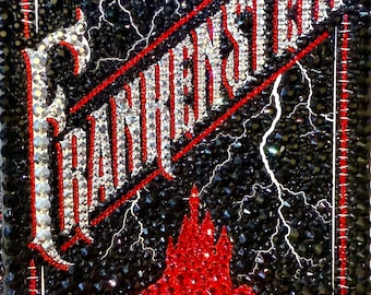 May include: A black and red embellished cover of "Frankenstein" by Mary Shelley. The title and author's name are in sparkling crystals. The background is black with white lightning bolts and a red castle.