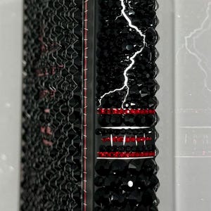 May include: Black book cover with the title "Frankenstein" in white. The spine is decorated with red and black crystals, and a white lightning bolt design. The cover is covered in black crystals.