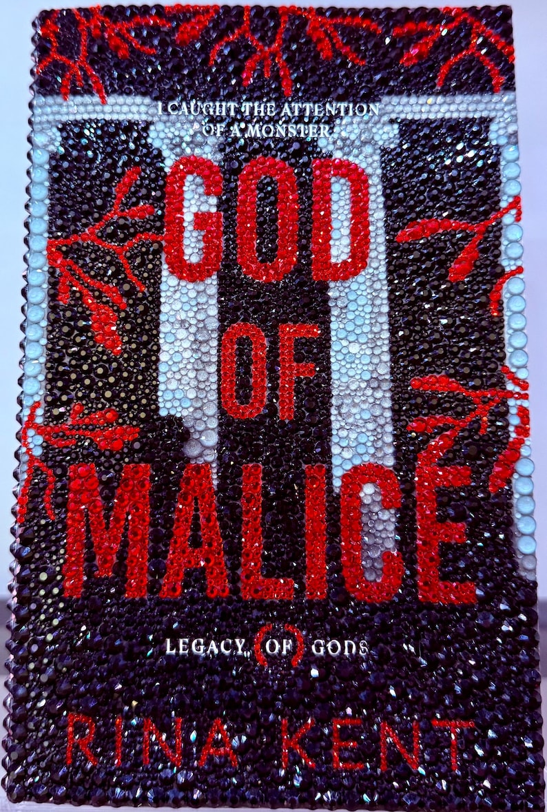 May include: A book cover with the title "GOD OF MALICE" in large red letters. The cover is black with a pattern of black and white vertical stripes and is embellished with sparkling crystals. The author's name, Rina Kent, is at the bottom.