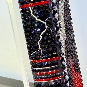 May include: A decorative book titled "Frankenstein" with a black cover adorned with red and black crystals. The spine features a lightning bolt design and the title in white lettering. The edges are also embellished.