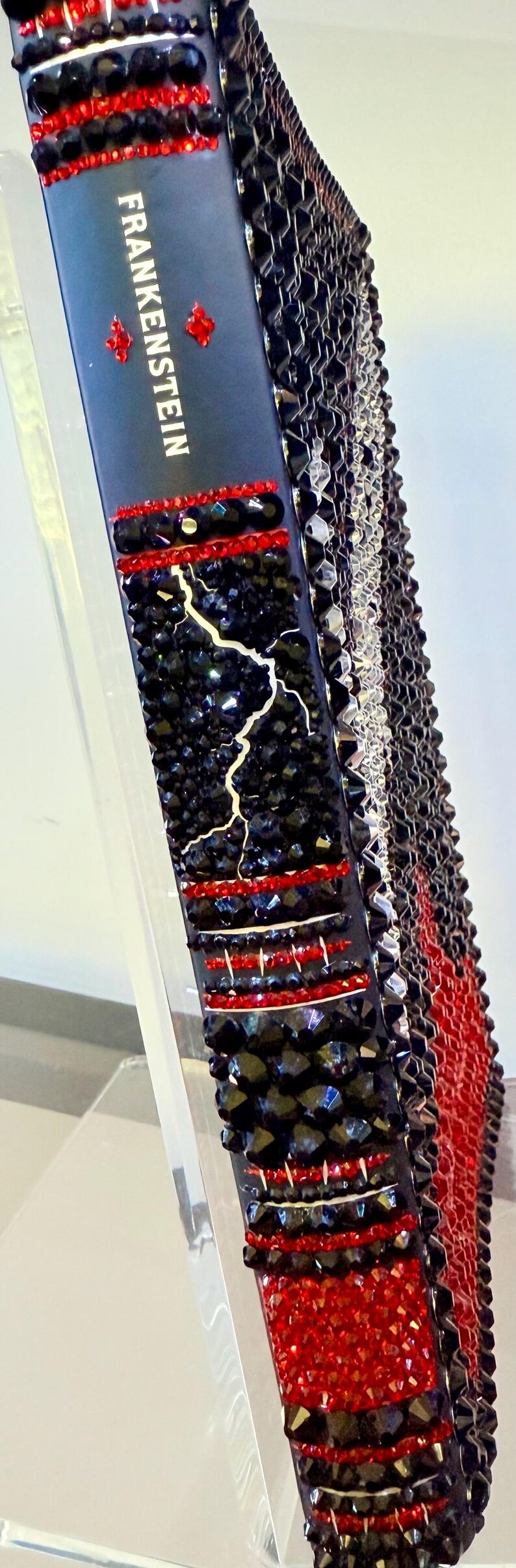 May include: A decorative book titled "Frankenstein" with a black cover adorned with red and black crystals. The spine features a lightning bolt design and the title in white lettering. The edges are also embellished.