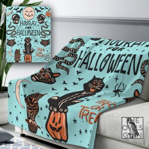May include: A blue and white Halloween themed throw blanket with black cats, owls, pumpkins, bats, and stars. The blanket has the text "Hooray for Halloween" and "Trick or Treat" printed on it.