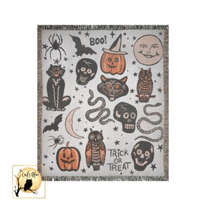 Puede incluir: Una manta tejida con fondo blanco y un patr&oacute;n repetido de iconos de Halloween. Los iconos incluyen un gato negro, una calavera, una serpiente, una calabaza, un b&uacute;ho, un murci&eacute;lago, una luna creciente y estrellas. El texto "Boo!" y "Trick or Treat" tambi&eacute;n est&aacute; incluido en el patr&oacute;n.
