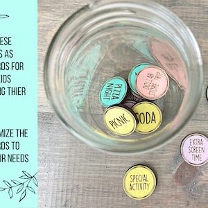 Puede incluir: Un tarro de vidrio lleno de fichas de madera de colores con frases como "Pizza Night", "Dollar Store Trip", "Picnic", y "Soda". Tambi&eacute;n hay fichas fuera del tarro que dicen "You Pick Dinner", "Extra Screen Time", y "Special Activity".