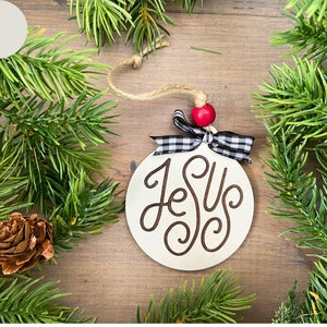 Jesus ornament with red bow and plaid ribbon and greenery.