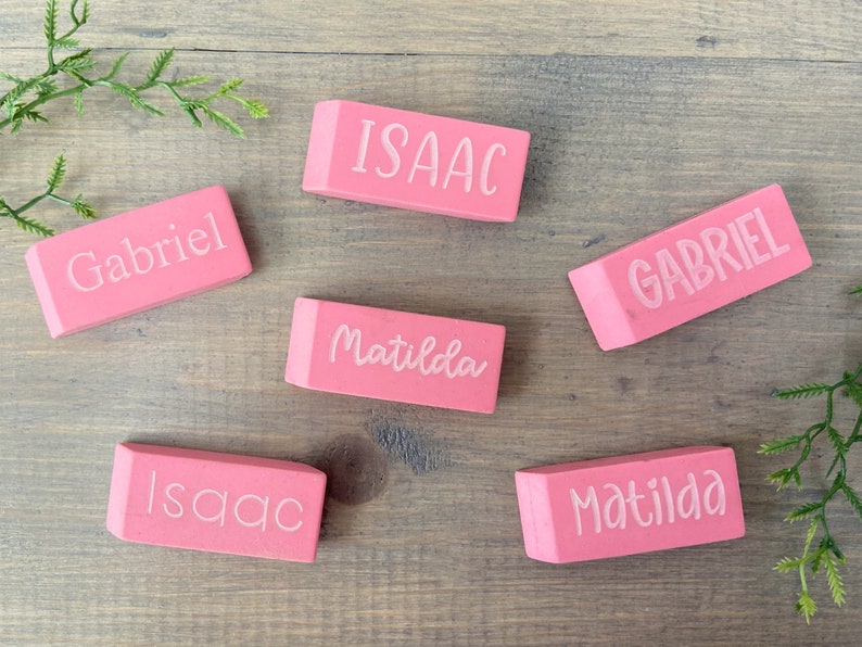May include: Six pink rectangular erasers with white lettering. The names "Isaac", "Gabriel", and "Matilda" are written on the erasers.
