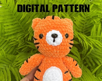 May include: A crocheted orange and black tiger plush toy with white accents. The toy has a cute, cartoon-like face and is holding a small white heart.