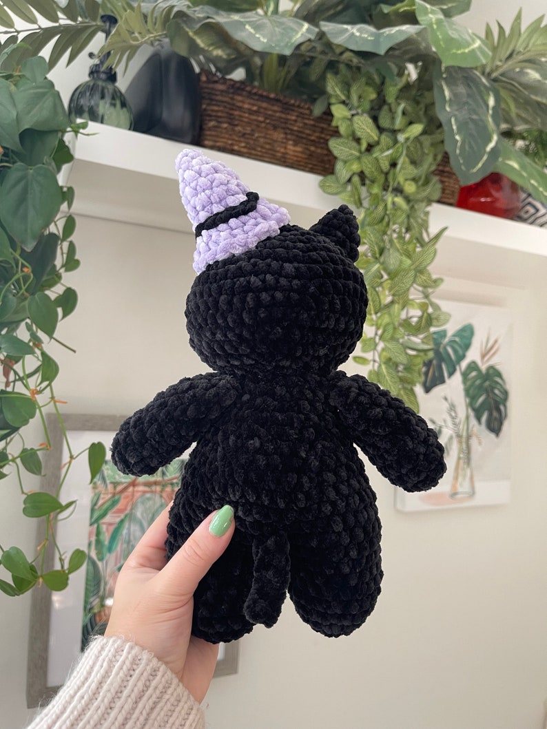 May include: Black crocheted cat plush toy wearing a purple and black witch hat.