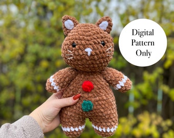 May include: A brown crocheted gingerbread cat plush toy with white accents and red and green buttons.  The toy is being held in a hand.  Digital Pattern Only.