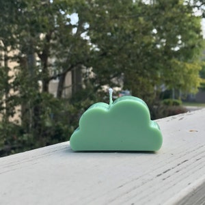 May include: A green cloud-shaped candle with a white wick.