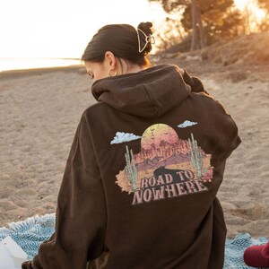 May include: Brown hooded sweatshirt with a graphic print of a desert landscape and the text "Road to Nowhere".
