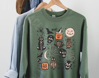 May include: A green sweatshirt with a vintage Halloween print featuring a black cat, owl, pumpkins, skulls, bats, and a snake. The text "Boo!" and "Trick or Treat" are also included in the design.
