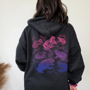 May include: Black hooded sweatshirt with a graphic print of frogs in shades of pink and purple on the back.