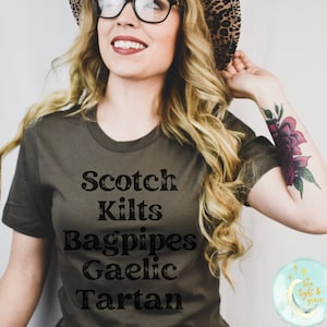 May include: A woman wearing a green t-shirt with the words "Scotch Kilts Bagpipes Gaelic Tartan" printed on it.