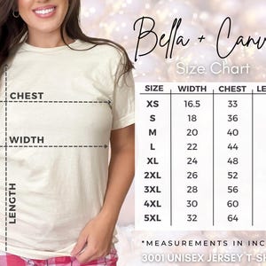 Peut inclure: Une femme porte un t-shirt unisexe Bella + Canvas 3001 de couleur cr&egrave;me. L'image comprend un tableau des tailles avec des mesures en pouces pour la largeur, la poitrine et la longueur, allant de XS &agrave; 5XL.