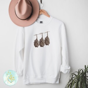 May include: White sweatshirt with a graphic of three brown bats hanging upside down on a line.