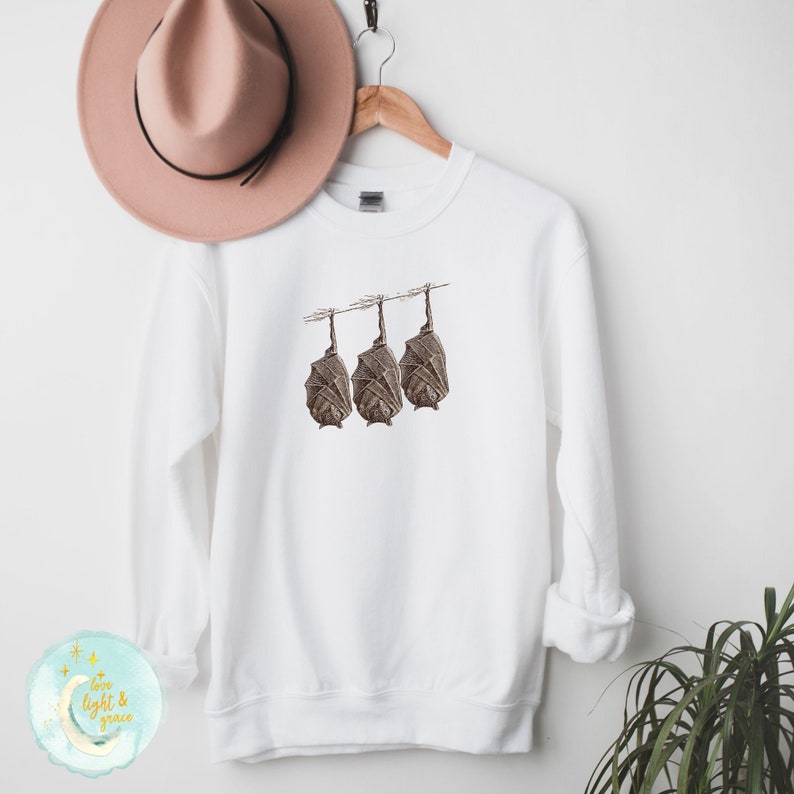 May include: White sweatshirt with a graphic of three brown bats hanging upside down on a line.