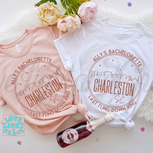 May include: Two pink and white t-shirts with a brown circle design that says "Ally's Bachelorette Charleston SC Last Fling Down King".
