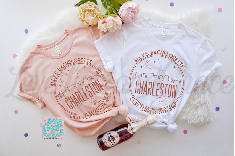 May include: Two pink and white t-shirts with a brown circle design that says "Ally's Bachelorette Charleston SC Last Fling Down King".