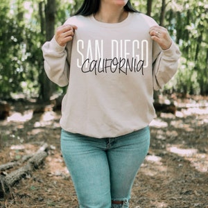 May include: A beige sweatshirt with the text "SAN DIEGO CALIFORNIA" printed in white on the front.