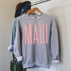 Peut inclure: Sweat-shirt gris avec un motif rose "MAUI" sur le devant.