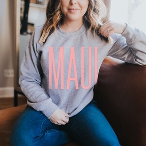 Peut inclure: Un sweat-shirt gris avec le mot "MAUI" imprim&eacute; en rose sur le devant.
