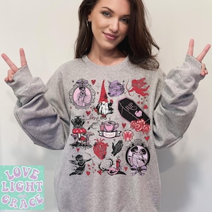 May include: A light gray sweatshirt with a variety of gothic-themed illustrations, including a skeleton, gnome, wolf, and cherub. The sweatshirt also features the text "Love Light and Grace" in a pastel green font.