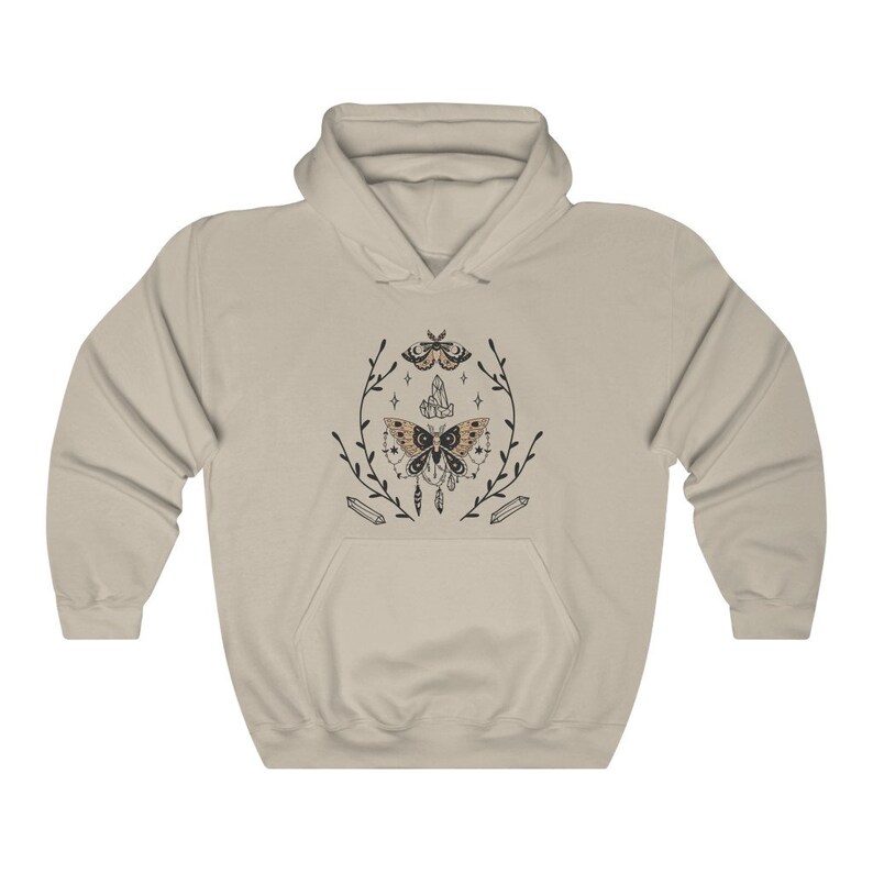 Puede incluir: Una sudadera con capucha beige con un estampado gr&aacute;fico de una polilla con cristales y plumas. La polilla est&aacute; rodeada de una corona floral.