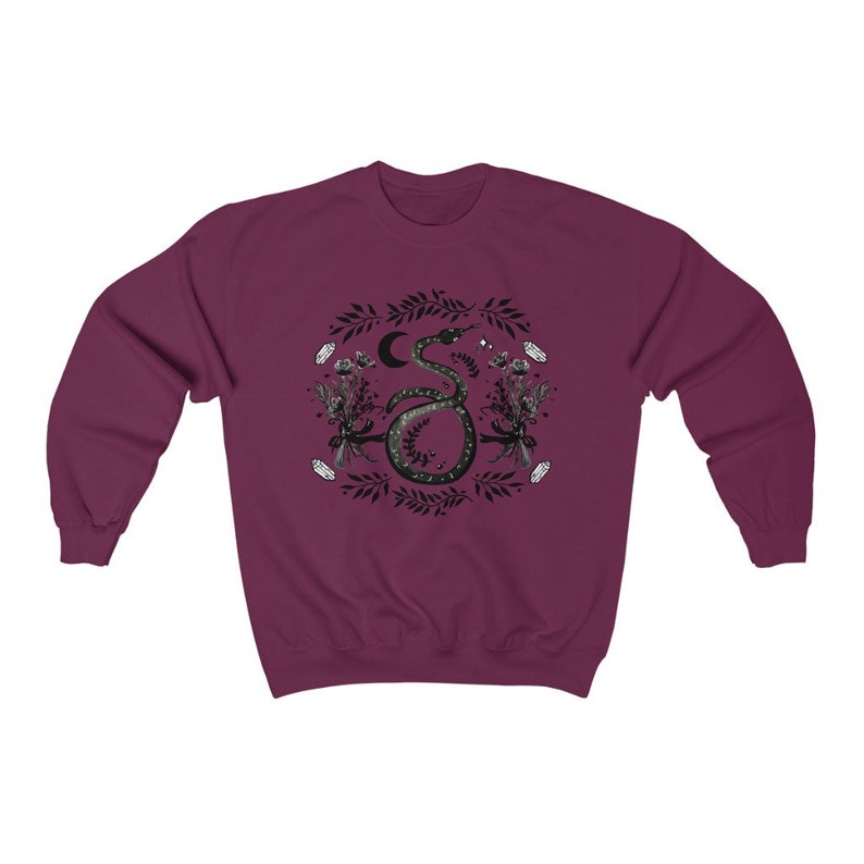 May include: A maroon sweatshirt with a black and white graphic print of a snake with a crescent moon and stars. The snake is surrounded by floral and leaf designs.