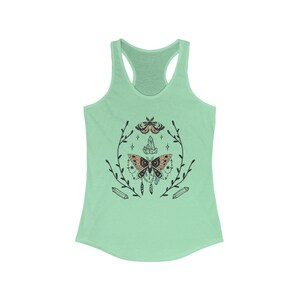 May include: A mint green tank top featuring a black and brown moth design. The moth is surrounded by a wreath of leaves and crystals.