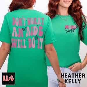 Peut inclure: T-shirts verts avec des textes et des graphiques de papillons. Un t-shirt porte l'inscription "DON'T WORRY AN AIDE WILL DO IT" au dos. L'autre t-shirt porte l'inscription "Miss Smith" sur le devant. Le texte est rose et blanc.