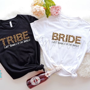 May include: Two white t-shirts with black text that says "BRIDE" and "TRIBE" in leopard print. The text also says "Last Rumble in the Jungle!" on both shirts.