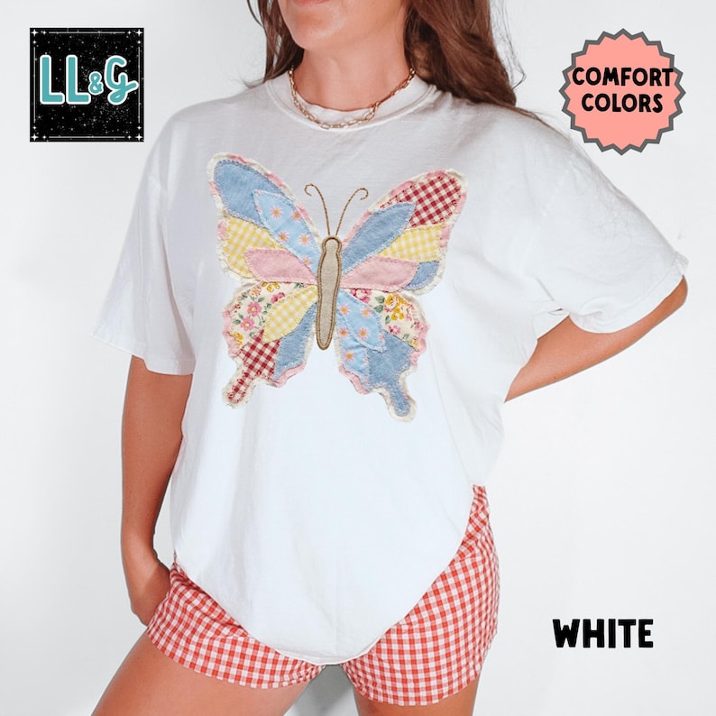 Peut inclure: T-shirt blanc avec un motif de papillon patchwork color&eacute;. Le papillon pr&eacute;sente des tissus bleus, roses, jaunes et &agrave; motifs floraux. Le t-shirt porte les mentions "COMFORT COLORS" et "WHITE". Le logo de la marque "LL&G" est en haut &agrave; gauche.