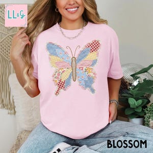 Peut inclure: T-shirt rose clair avec un motif papillon en patchwork. Le papillon est compos&eacute; de diff&eacute;rents tissus aux couleurs bleu, rose, jaune et rouge. Le mot "BLOSSOM" est imprim&eacute; en noir en bas du t-shirt.