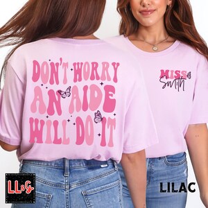 Peut inclure: T-shirts lilas avec le texte "DON'T WORRY AN AIDE WILL DO IT" en rose, avec des graphiques de papillons. Le devant du t-shirt porte l'inscription "Miss Smith" en rose. Les t-shirts sont de couleur violet clair.