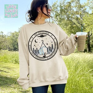 May include: A beige sweatshirt with a black and white graphic print of a mountain, a UFO, and stars. The text on the graphic reads "Go Outside Worst Case Scenario, Aliens Abduct You."