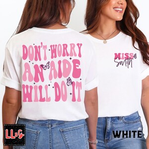 Peut inclure: T-shirts blancs avec des textes roses et des graphiques de papillons. Un t-shirt porte l'inscription "DON'T WORRY AN AIDE WILL DO IT" au dos. L'autre t-shirt porte l'inscription "Miss Smith" sur le devant. Les deux t-shirts sont associ&eacute;s &agrave; des jeans bleus.