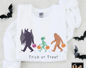 May include: White sweatshirt with a Halloween-themed graphic. The design features a bat-winged creature, an alien, and a Bigfoot walking and carrying pumpkin-shaped treat bags. The words "Trick or Treat" are printed below the figures.