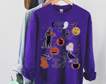May include: A purple sweatshirt featuring Halloween-themed graphics. The design includes a black cat playing a violin, a ghost, a witch on a broom, pumpkins, bats, and the words "Trick or Treat".