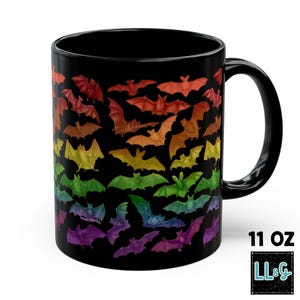 May include: A black ceramic mug with a capacity of 11 oz, featuring a repeating pattern of bats in a rainbow gradient of colors including red, orange, yellow, green, blue, and purple against a solid black background with a curved handle.