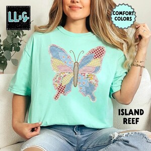 Peut inclure: T-shirt vert clair avec un grand papillon appliqu&eacute;. Le papillon a des ailes en patchwork aux motifs bleus, roses, jaunes et rouges. Le t-shirt porte les mentions "COMFORT COLORS" et "ISLAND REEF". Le logo de la marque "LL&G" est en haut &agrave; gauche.